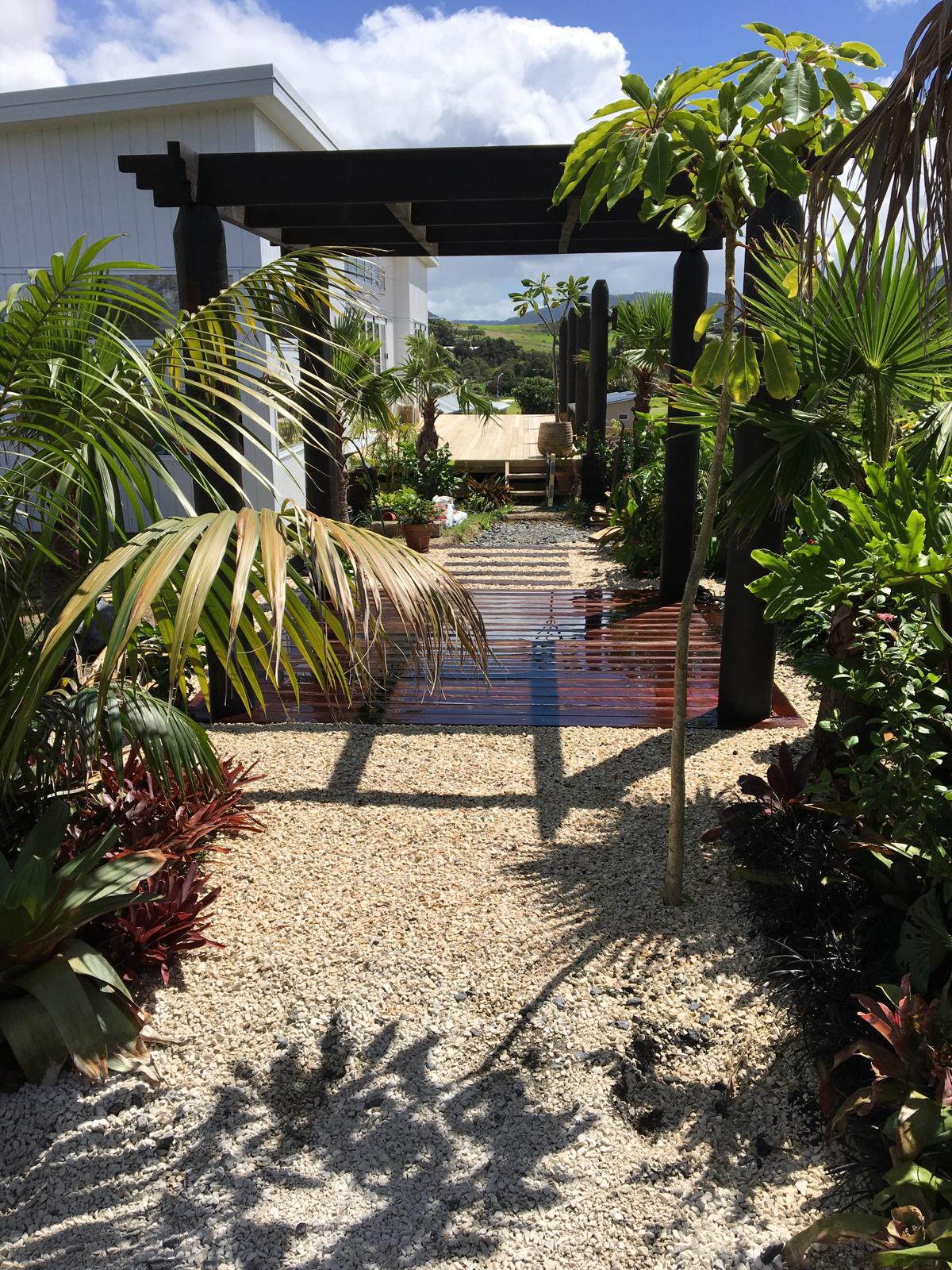 Tropical entrance pathway with timber pergola, polished hardwood deck, white pebble courtyard and lush palms