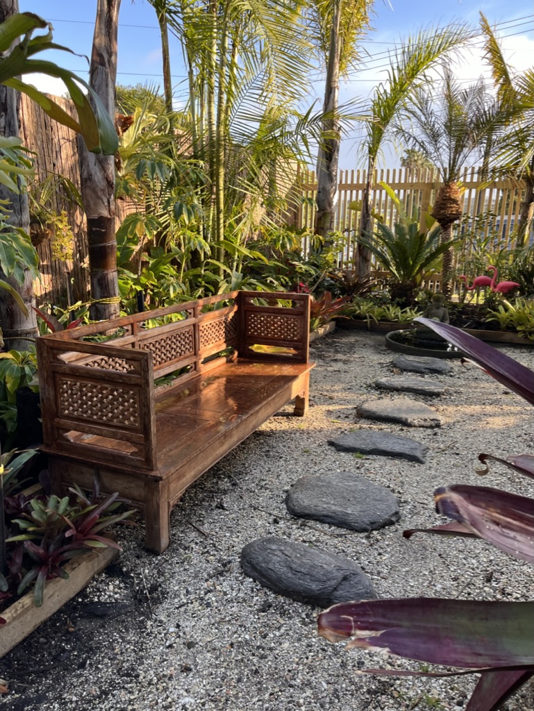 Tropical garden with carved timber bench, stepping stones and lush palms